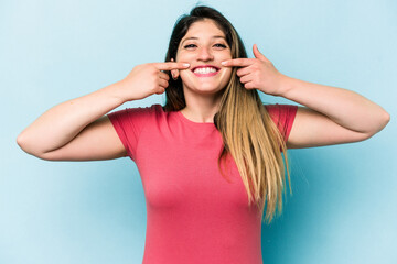 Young caucasian woman isolated on blue background smiles, pointing fingers at mouth.