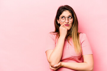 Young caucasian woman isolated on pink background relaxed thinking about something looking at a copy space.