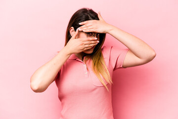 Obraz premium Young caucasian woman isolated on pink background blink at the camera through fingers, embarrassed covering face.