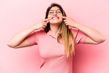 Naklejka premium Young caucasian woman isolated on pink background smiles, pointing fingers at mouth.