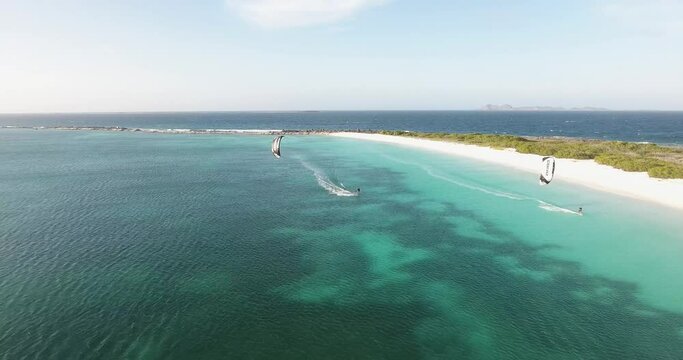 Two Kitesurfers fly along tropical Coastline Crasqui Island, Aerial view dolly out Los Roques 