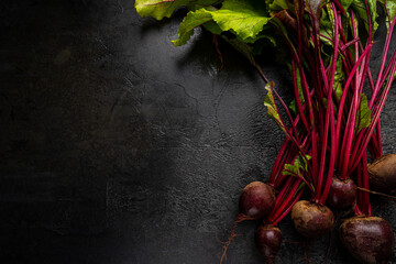 Fresh red beetroot with herbage green leaves over black background, top view