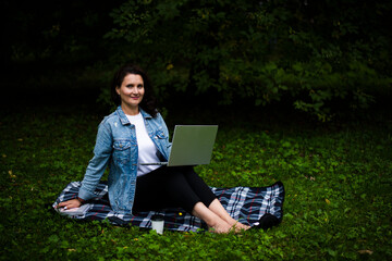 Young beautiful girl student in denim clothes works in the park on a laptop