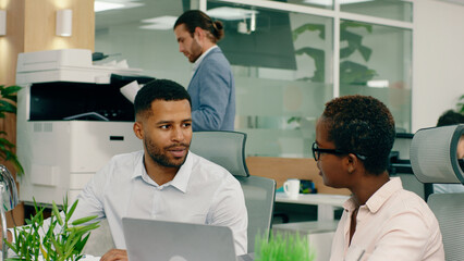 Two african workers are at the modern office and they are sitting at their desks smiling and...