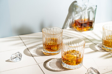 Whiskey with ice in glasses and bottle, white background with hard light, shadows and sun glare,...