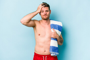 Young caucasian man holding beach towel isolated on blue background being shocked, she has...