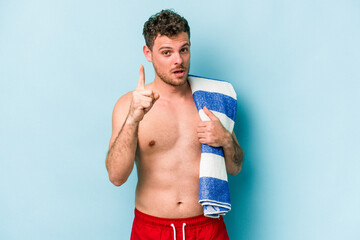 Young caucasian man holding beach towel isolated on blue background having an idea, inspiration concept.