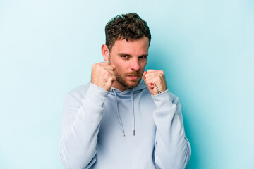 Young caucasian man isolated on blue background throwing a punch, anger, fighting due to an argument, boxing.