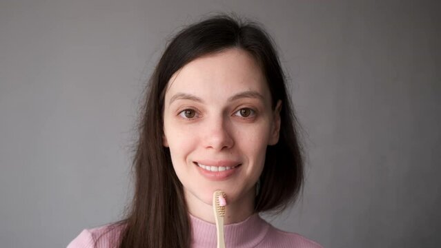 Smiling young brunette woman with organic bamboo toothbrush and toothpaste in her hands. Biodegradable ecological personal care products. Plastic free lifestyle concept.