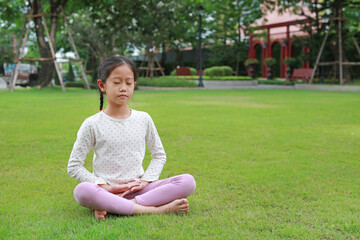 Asian young girl child practicing mindfulness meditation sitting on lawn in the garden. Peaceful concept.