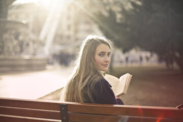 young woman reads a book sitting on a bench - 507862763