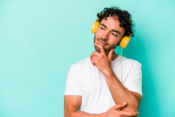 Young caucasian man listening to music isolated on blue background relaxed thinking about something...