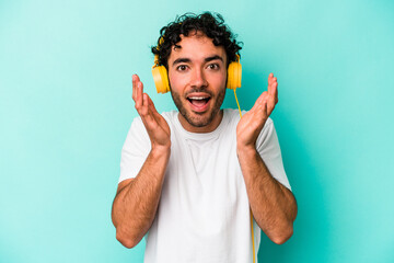 Young caucasian man listening to music isolated on blue background receiving a pleasant surprise, excited and raising hands.