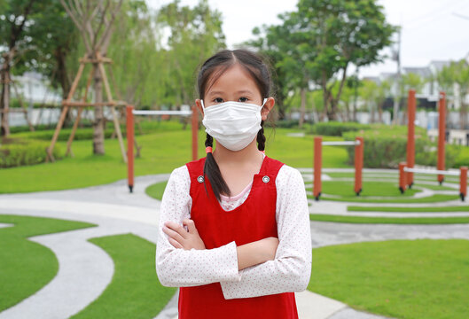Portrait of Asian girl child cross one's arm with wearing medical mask for protect covid-19 while stay in the garden.