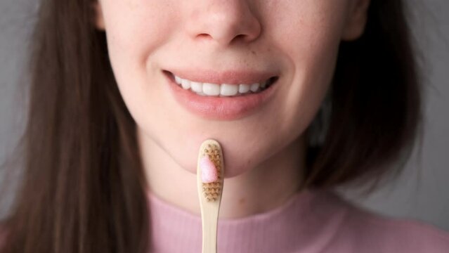 Smiling young brunette woman with organic bamboo toothbrush and toothpaste in her hands. Biodegradable ecological personal care products. Plastic free lifestyle concept.
