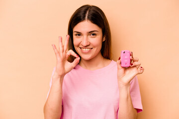 Young hispanic woman holding a keys car isolated on beige background cheerful and confident showing ok gesture.