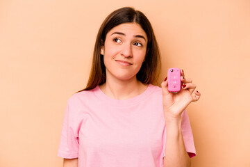 Young hispanic woman holding a keys car isolated on beige background dreaming of achieving goals and purposes