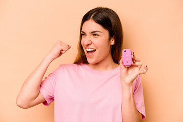 Young hispanic woman holding a keys car isolated on beige background raising fist after a victory, winner concept.