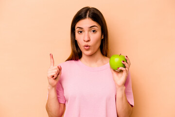 Young hispanic woman holding an apple isolated on beige background having some great idea, concept of creativity.