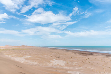 Dunes in front of the beach with the blue sky in the background and the horizon in the sea with some clouds.