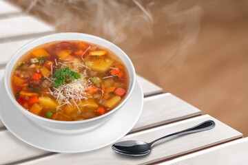 Tasty clear soup with beef slices and vegetables. Served in bowl on desk