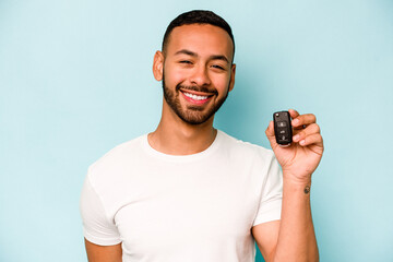 Young hispanic man holding car keys isolated on blue background laughing and having fun.
