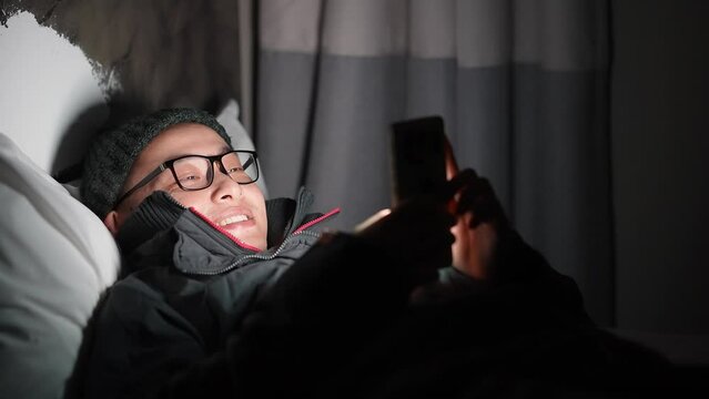 young chinese man lying and playing with mobile phone at night
