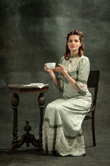 Vintage portrait of young beautiful girl in gray dress of medieval style drinking tea isolated on...
