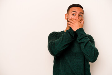Young hispanic man isolated on white background thoughtful looking to a copy space covering mouth with hand.