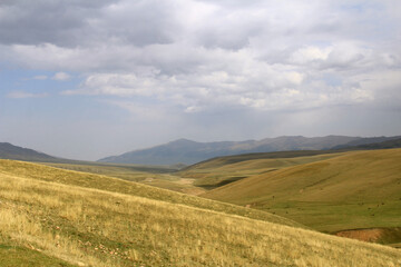 Steppe and hilly landscape with a view of the mountain ranges on the Assy plateau in autumn against the background of the sky with clouds, panorama