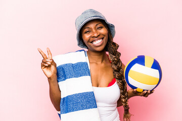 Young African American woman playing volleyball on a beach isolated on pink background joyful and...