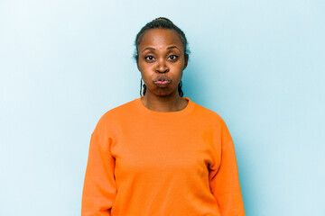 Young african american woman isolated on blue background blows cheeks, has tired expression. Facial expression concept.
