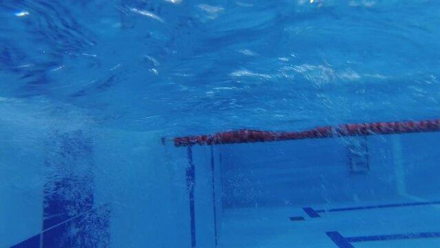 sportswoman swimmer in a tracksuit, in diving goggles, in a swimming cap is training in the pool. The athlete swims underwater. Underwater shooting, wide angle, 4k