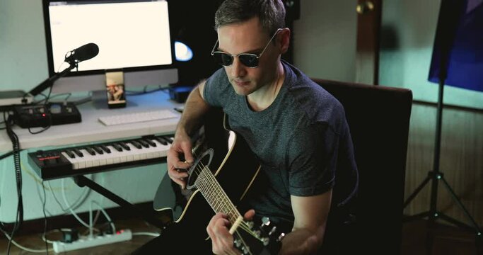 Music producer strumming some chords with the acoustic guitar while recording a new project at his home studio
