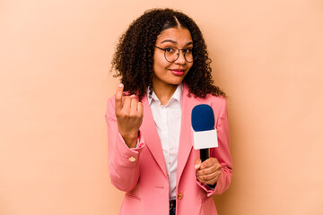 Young African American TV presenter woman isolated on beige background pointing with finger at you...