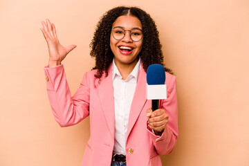 Young African American TV presenter woman isolated on beige background receiving a pleasant surprise, excited and raising hands. - obrazy, fototapety, plakaty