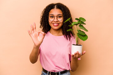 Young African American woman holding a plant isolated on beige background cheerful and confident...