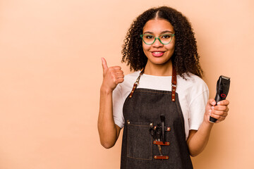 Young African American hairdresser woman isolated on beige background smiling and raising thumb up