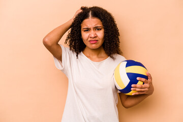 Young African American woman playing volleyball isolated on beige background being shocked, she has...