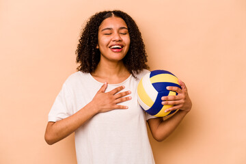 Young African American woman playing volleyball isolated on beige background laughs out loudly keeping hand on chest.