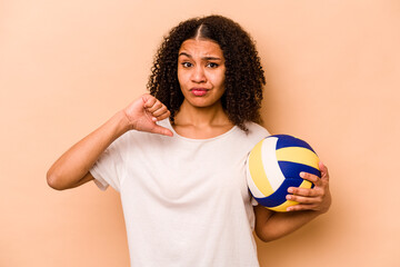 Young African American woman playing volleyball isolated on beige background feels proud and self...