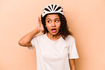 Young hispanic woman wearing a helmet bike isolated on blue background trying to listening a gossip.