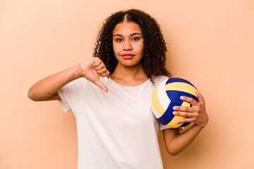 Young African American woman playing volleyball isolated on beige background showing a dislike...