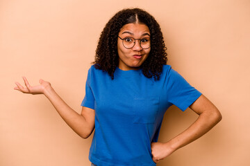 Young African American woman isolated on beige background doubting and shrugging shoulders in...