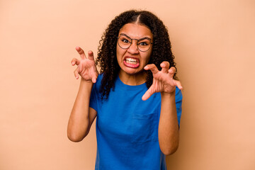 Young African American woman isolated on beige background upset screaming with tense hands.