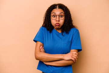 Young African American woman isolated on beige background blows cheeks, has tired expression....