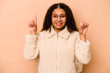 Young African American woman isolated on beige background indicates with both fore fingers up...