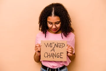 Foto op Canvas Young African american woman holding we need a change placard isolated on beige background © Asier