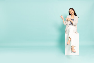 Young Asian businesswoman sitting and pointing to empty copy space isolated on green background - 507868302