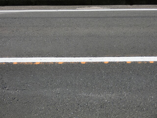 古い黄色のセンターラインの上に白い実線のセンターラインが引かれた片側一車線の道路